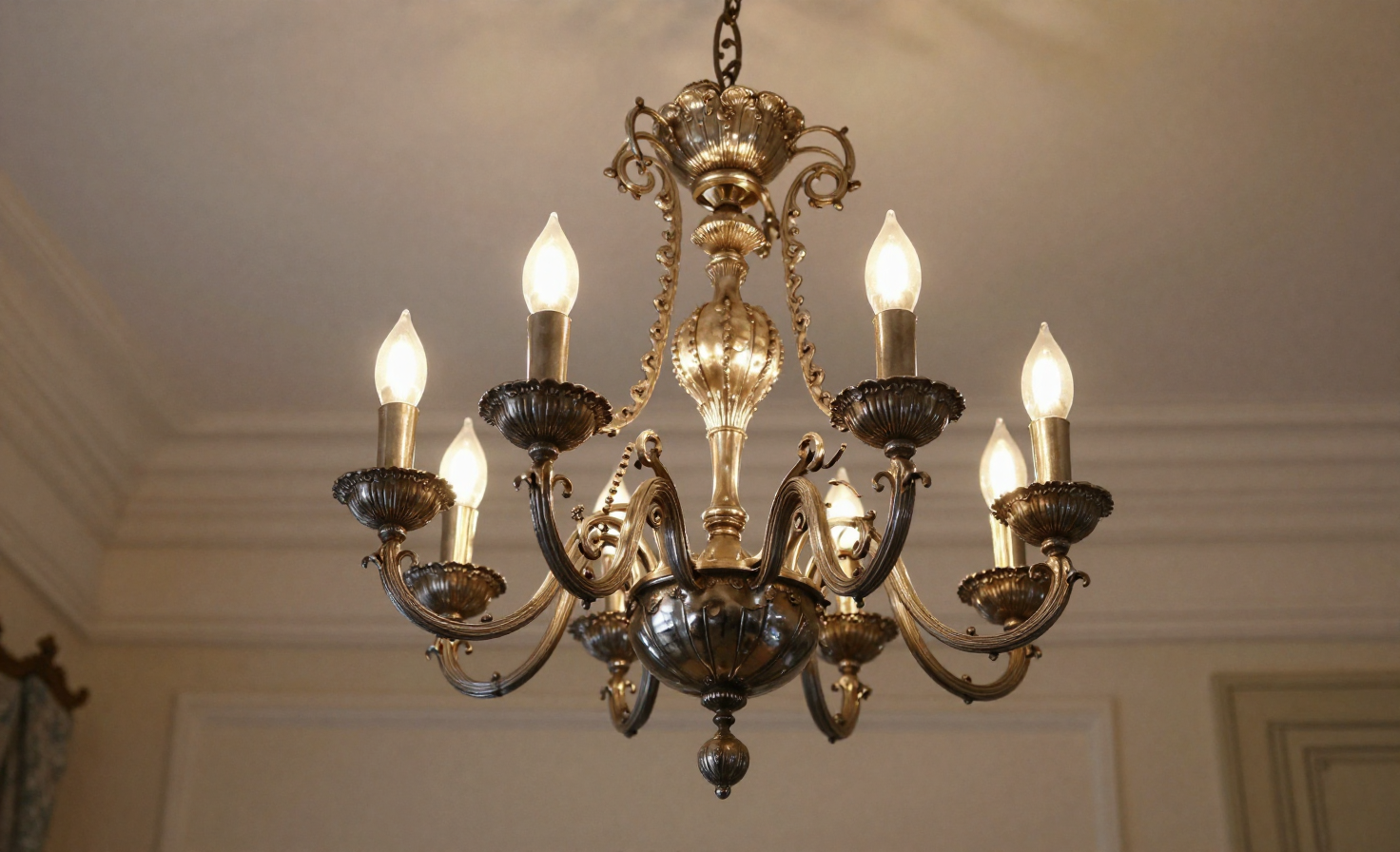 A silver chandelier with intricate metalwork and a warm bronze patina, hanging from the ceiling.