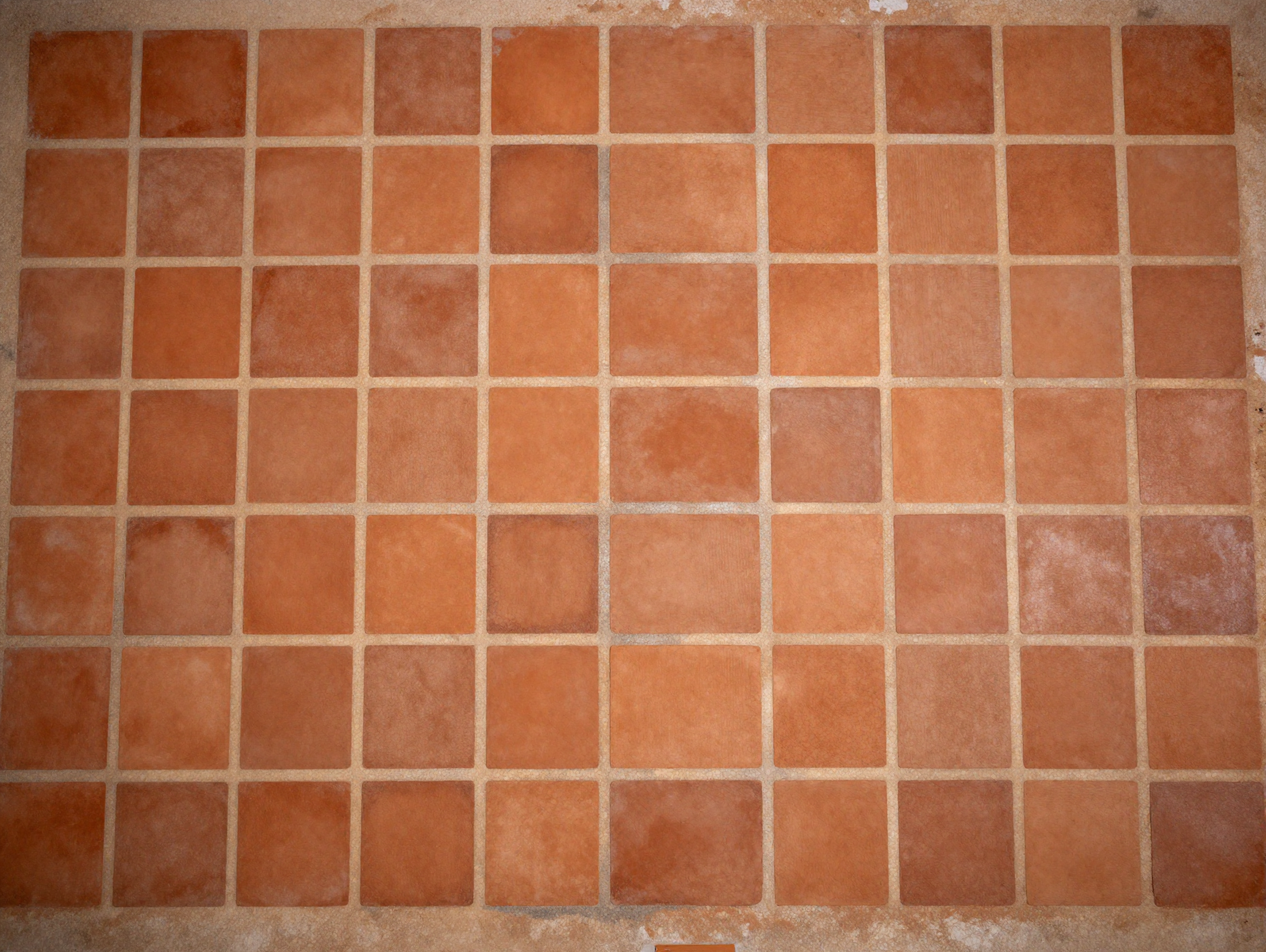 Top-down view of a floor made of square terracotta tiles with thin mortar joints.