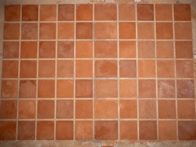 Top-down view of a floor made of square terracotta tiles with light mortar joints.