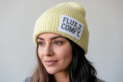 A woman wearing a pale yellow beanie with a patch that says "FLUX.2 COMFY".