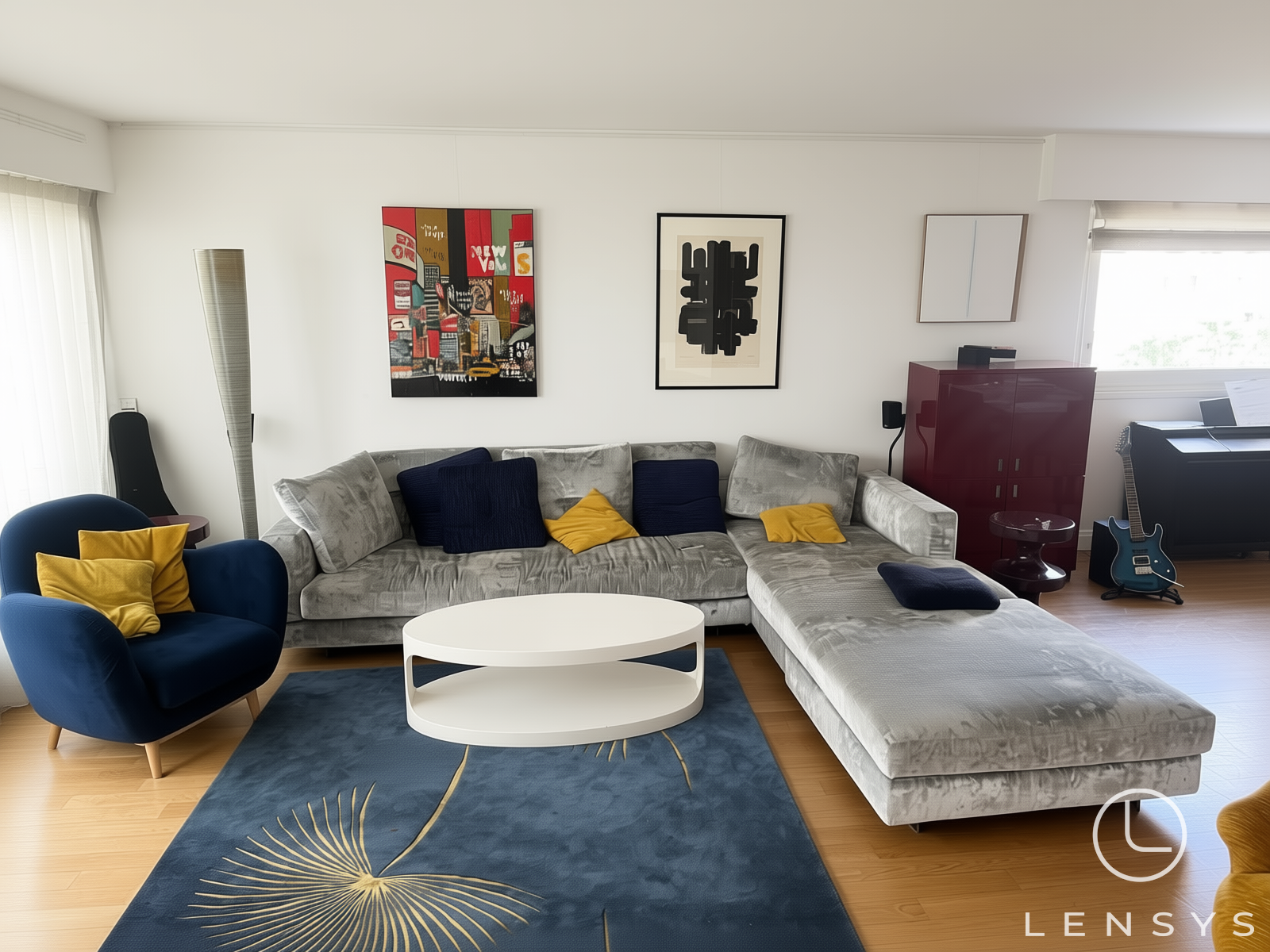 A bright, clean living room featuring a large grey L-shaped sectional sofa, a blue armchair, a white coffee table, and a blue rug with a gold botanical design.