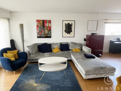A modern living room with a gray sectional sofa, blue armchair, and artwork.
