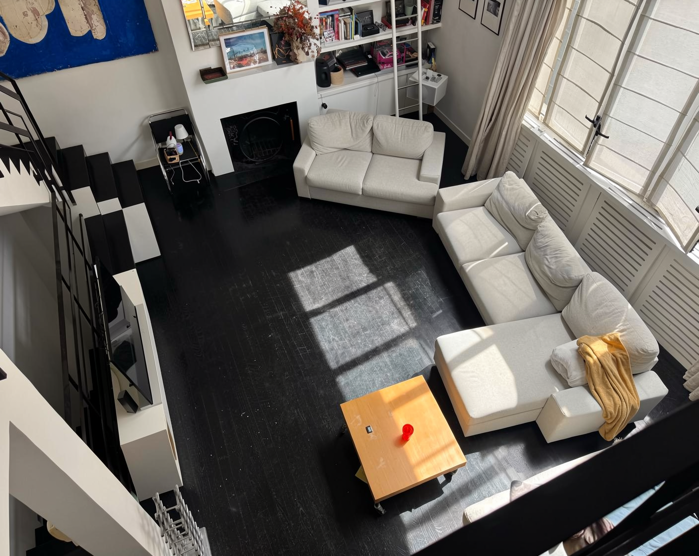 High-angle shot of a modern living room with white sofas, black floors, and a staircase.