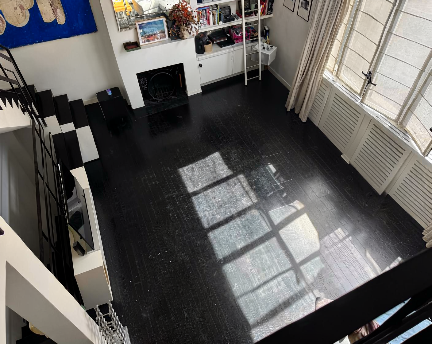 High-angle view of an empty room with dark wooden floors and a large window.