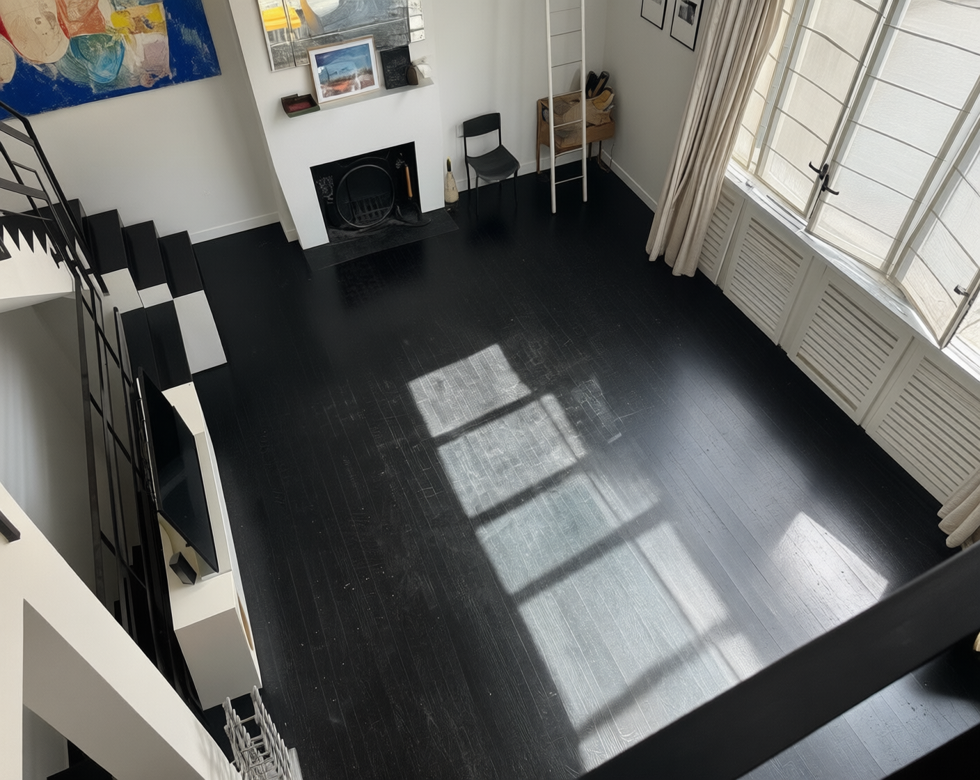 An empty, modern loft interior with dark wood floors, white walls, a black and white staircase, and large windows with natural light.