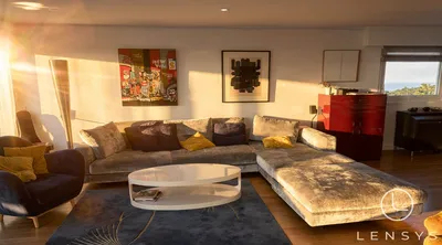 A modern living room bathed in warm sunlight, featuring a large sectional sofa, artwork, and a coffee table.