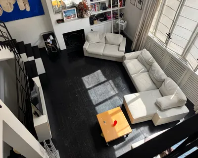 High-angle view of a modern living room with black floors, white sofas, and large windows.