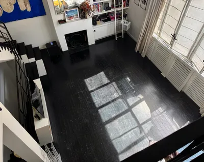 High-angle view of an empty room with dark wooden floors and a large window.