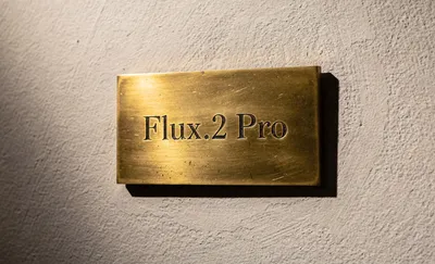 A rectangular brass plaque with "Flux.2 Pro" engraved in serif font, mounted on a textured off-white wall with soft lighting from the left.